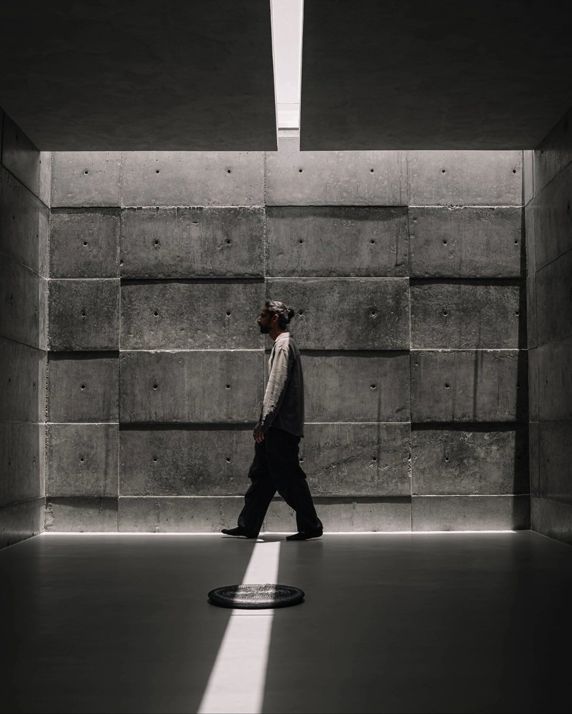 A figure walking through a concrete hall cut by a slit of light