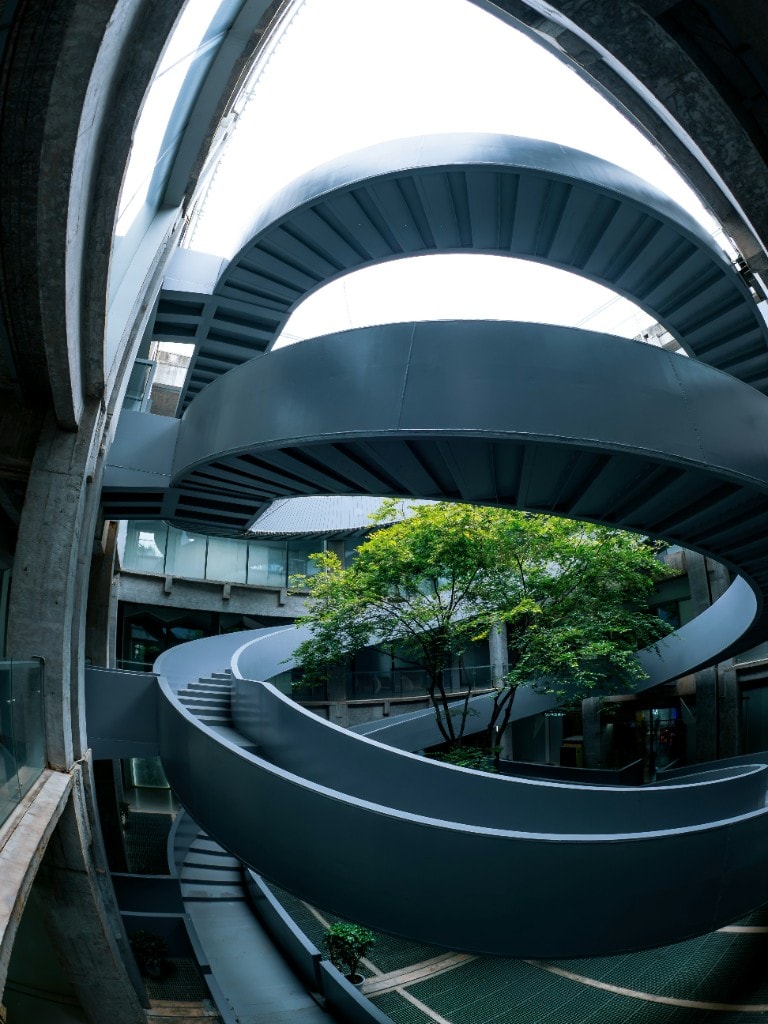 A steel atrium with spiral ramps and a tree at its centre